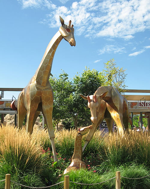 two modern-art metal sculptures of giraffes, in tall grass near the entrance to the Denver Zoo