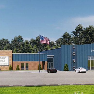 Photo of a blue and brown building with an American flag on a pole in the parking lot in front of it, The large letters L C R C are visible on the side of the building.